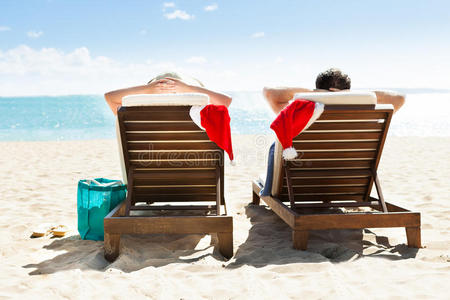 一对夫妇带着圣诞老人的帽子在海滩度假胜地的甲板椅上放松
