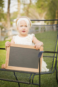 可爱的女婴坐在椅子上，拿着空白的黑板
