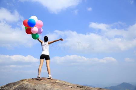 亚洲女人站在山顶岩石上，拿着五颜六色的气球