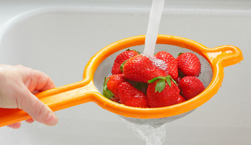 在用水冲洗的成熟草莓冻滴小女孩和男婴在厨房水槽里洗水果.