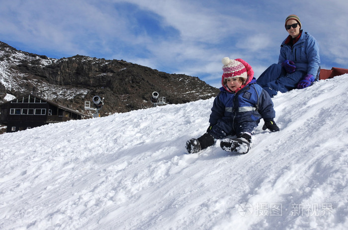 母亲看着她蹒跚学步的女孩在雪上的滑行