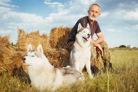 老胡子的男人坐在干草堆里与他们的狗,享受夏天日落景色.