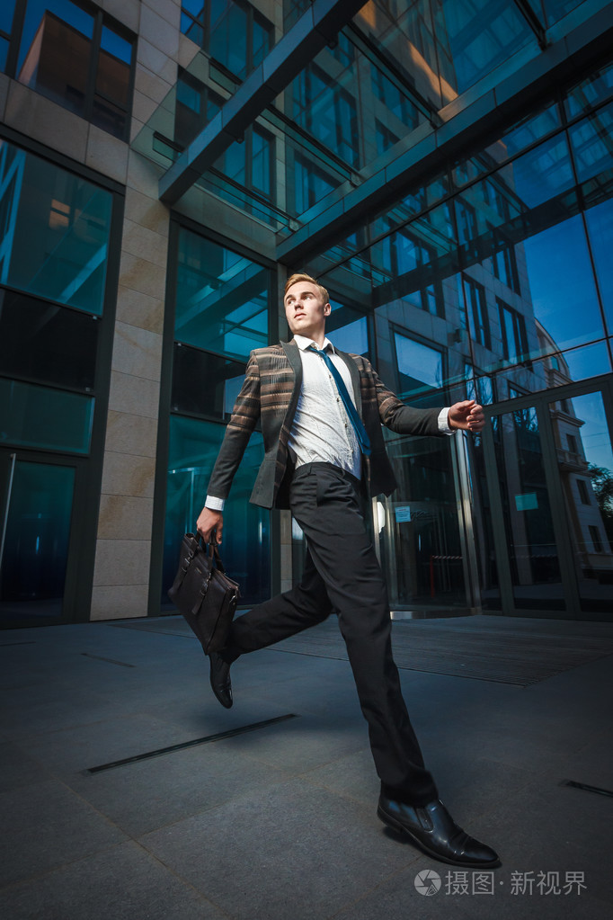 现代办公室附近运行的年轻英俊成功时尚商人