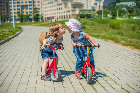幼儿男孩和女孩接吻在平衡中夏公园自行车照片