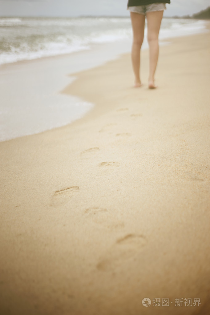 海滩旅行年轻女子走在沙滩上留下脚印在沙滩上特写镜头细节的女性脚和