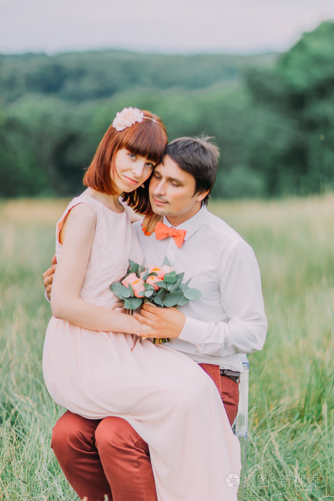 可爱年轻的红头新娘坐在新郎怀里看着相机中夏公园