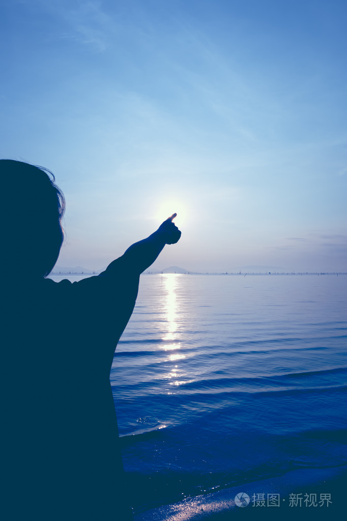 剪影后面观女人放松在海边和指向太阳