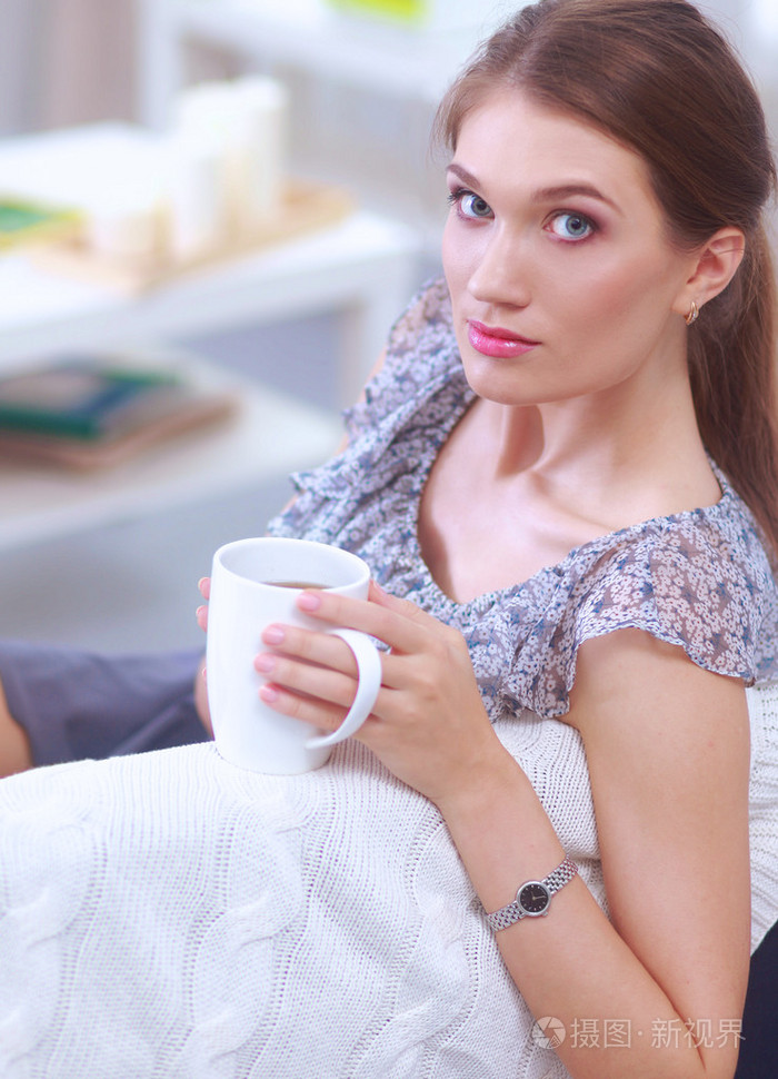 年轻漂亮的女人在家里的沙发上喝一杯的肖像