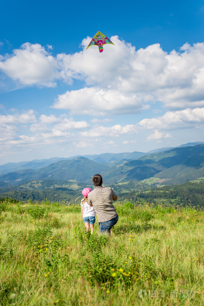 爸爸和女儿推出的美丽景色的山脉和天空背景下的风筝垂直
