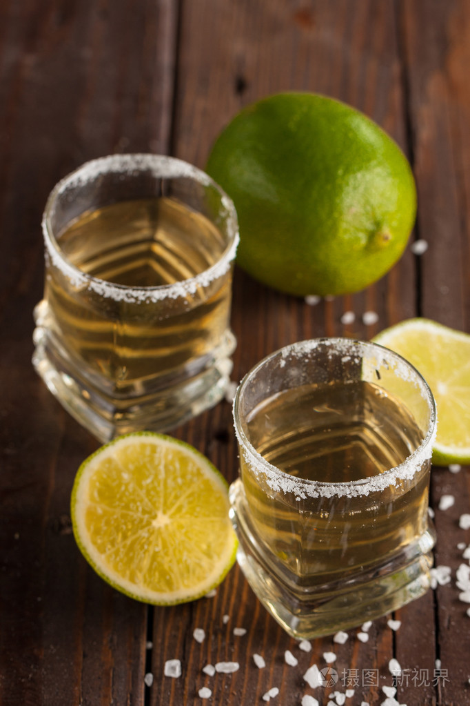 宏观焦点照片的黄金墨西哥龙舌兰与石灰和盐在木制背景。 酒精饮料的概念。
