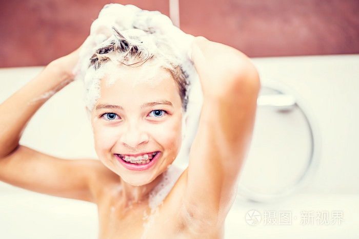 可爱的年轻女孩,在淋浴洗头发和脸上的洗发水.女孩戴着牙套