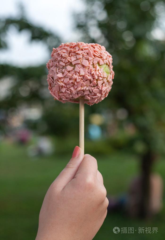 女人手里拿的糖果苹果与花生酱和草莓巧克力公园背景上照片-正版商用