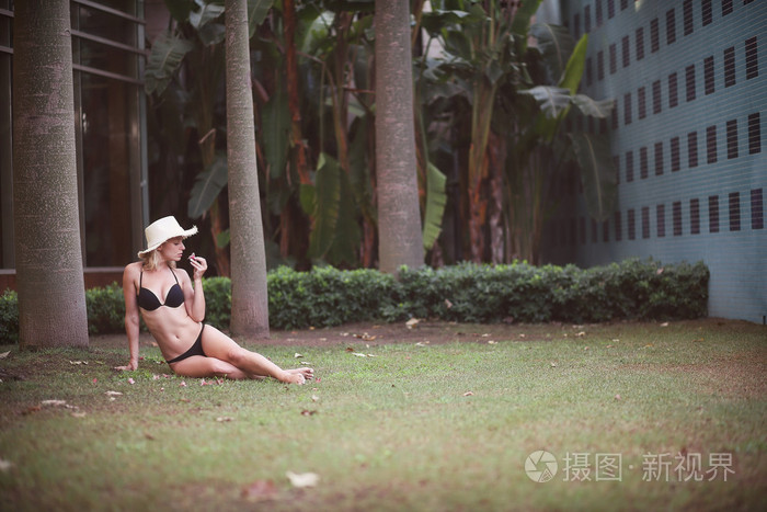 穿上泳衣，戴上帽子坐在草地上的女孩