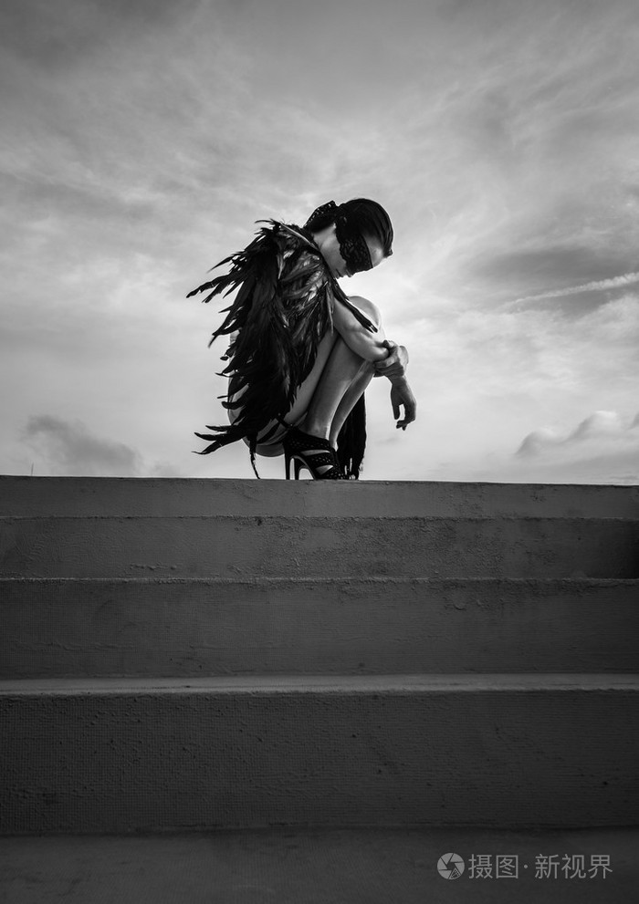 黑白照片的美丽诱人的天使女人与蒙着双眼穿着内衣和皮革腰带蹲在屋顶