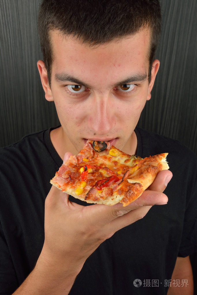 在深色背景上的贪婪的年轻人吃披萨的肖像