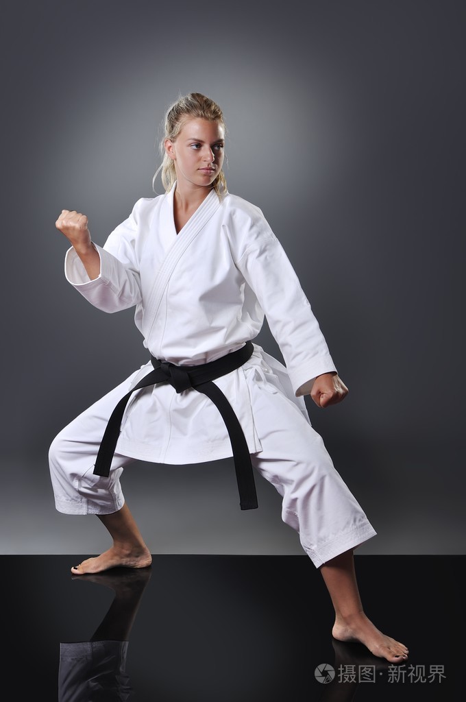 美丽年轻的黑带女空手道做卡塔在灰色的背景上