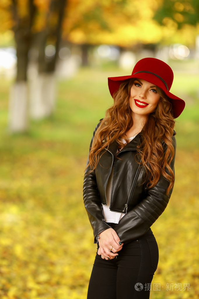 美丽优雅的女人站在时尚的红色帽子在一个公园在秋天里