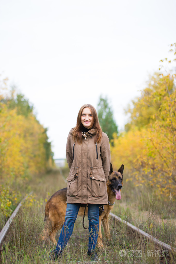 年轻可爱的女人与德国牧羊犬摆姿势的秋天预见