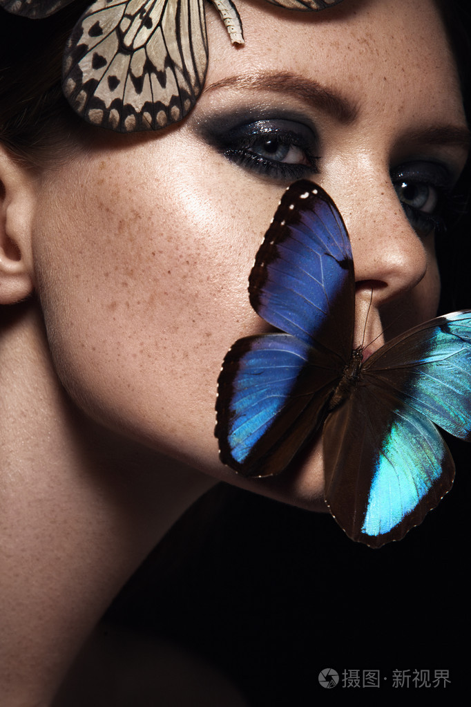 关闭了漂亮的化妆的女孩的画像蓝色的异国蝴蝶脸上有雀斑的脸