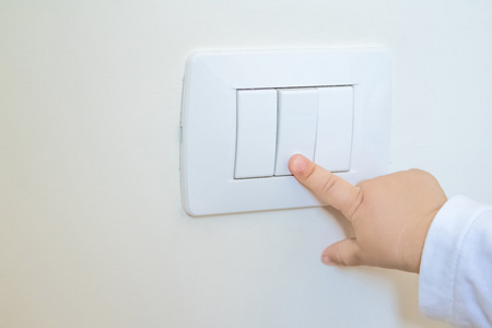 可爱的小男孩儿童拐弯处白色的灯开关,用他的手指的小手,新的一代概念
