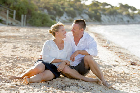 迷人的美丽情侣在浪漫的暑假坐在海滩上