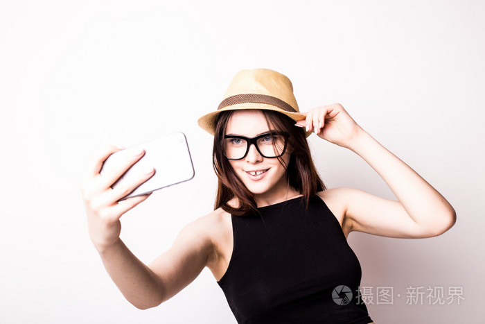 年轻漂亮姑娘把自拍照肖像照片用手机或相机太阳镜帽子和夏天在中穿别致时尚旅游