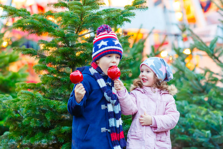 两个小孩子吃糖苹果上圣诞市场照片