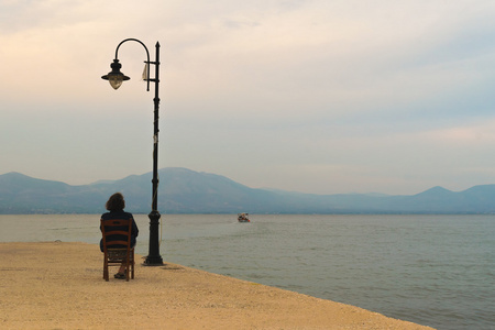 孤独的老妇人,看着一艘船离开港口对一个戏剧性的天空照片