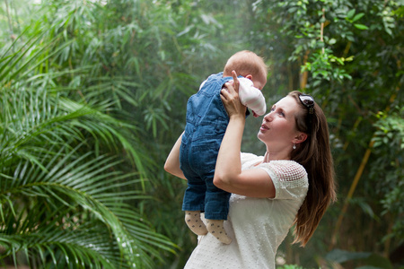 幸福的年轻女人抱着一个婴儿,在公园里散步照片
