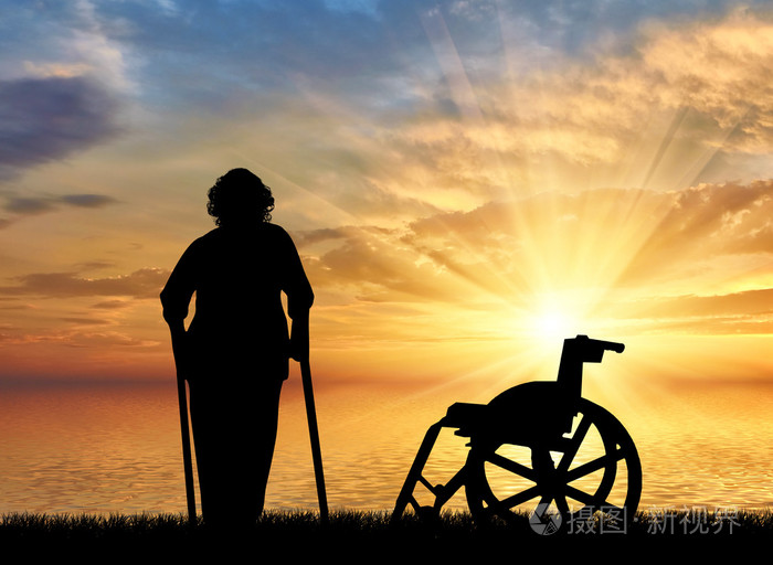 一位老太太拄着拐杖的海上日落和轮椅背景上的剪影