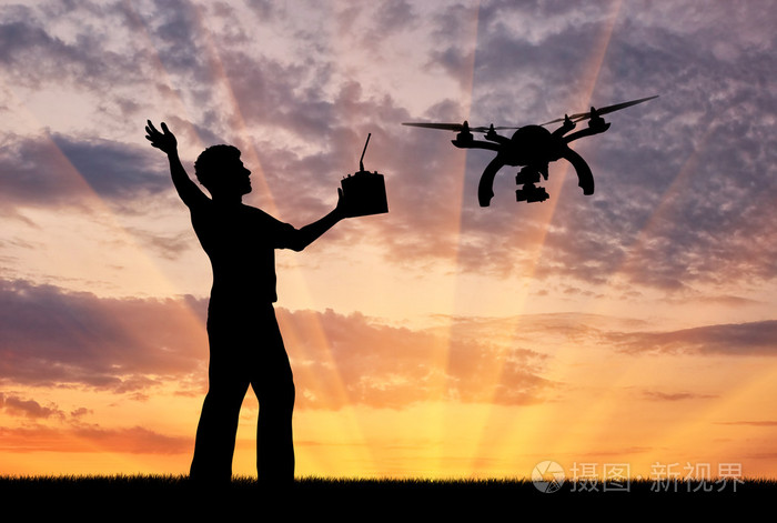 飞行的无人机,及一名男子用一个遥控器在日落时的剪影
