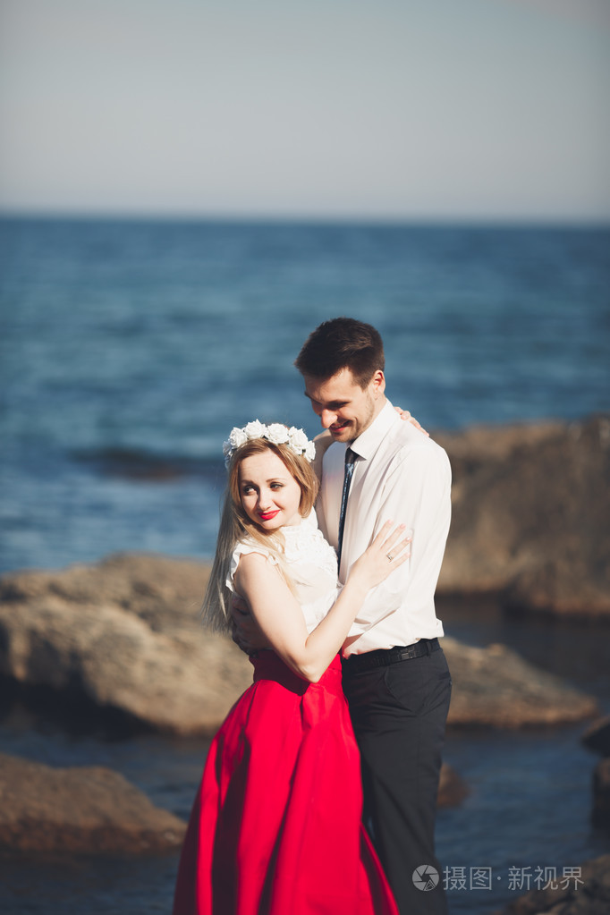 浪漫恩爱的夫妻靠近海蓝色天空的石头上摆姿势