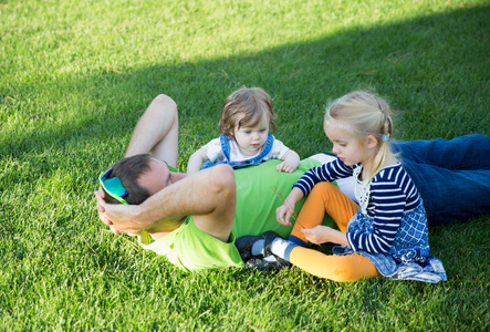 年轻的父亲带着两个女儿躺在公园的草地上照片