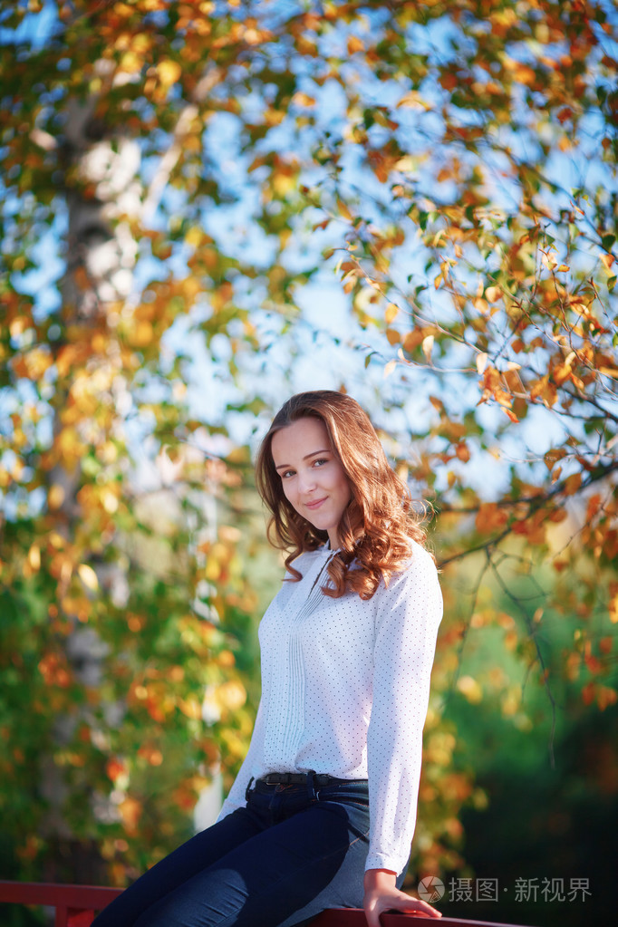 年轻漂亮的女人坐在多彩的秋天公园，垂直拍摄
