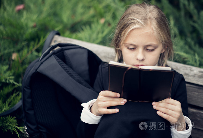 美丽的金发女孩,穿着校服坐在公园的长椅上,看书