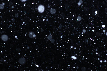 在黑色背景上的散景灯拍摄的飞片雪花在空中照片