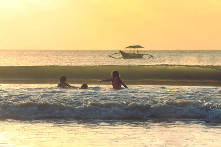 孩子们去游泳在金巴兰海滩的日落,在印度尼西亚巴厘岛照片