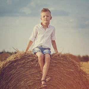 可爱的学龄前男孩坐在干草堆上