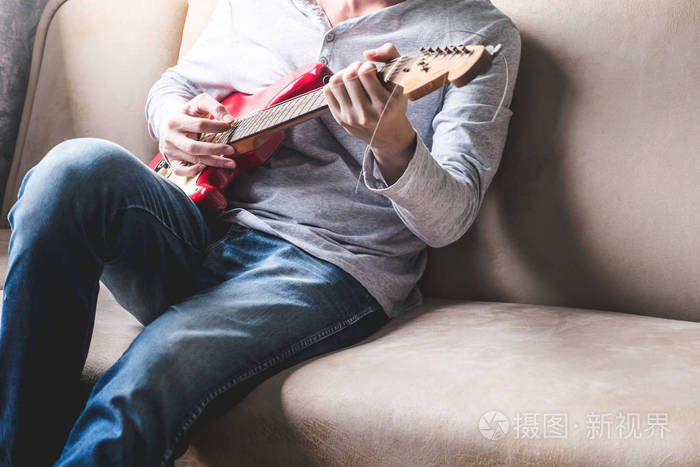 休闲的年轻男子在家里的沙发上弹吉他照片-正版商用图片1r4dvk-摄图新
