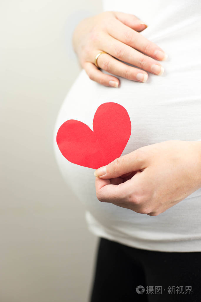 怀孕的女人捧在手红色的心孕妇腹中的胎儿关闭