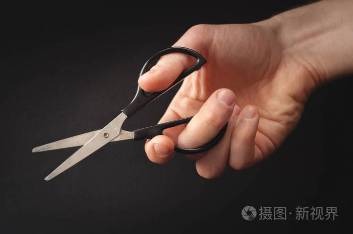 男手拿着一把小剪刀在黑色背景上的照片手