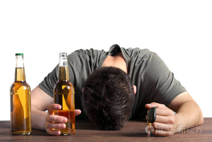 醉酒的年轻人把车钥匙和两瓶啤酒在灰色的背景上