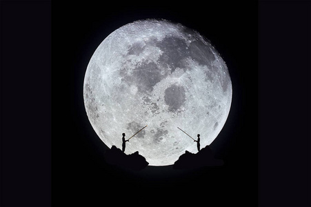 在超级月亮之夜,一个男人在岩石山上钓鱼的轮廓.