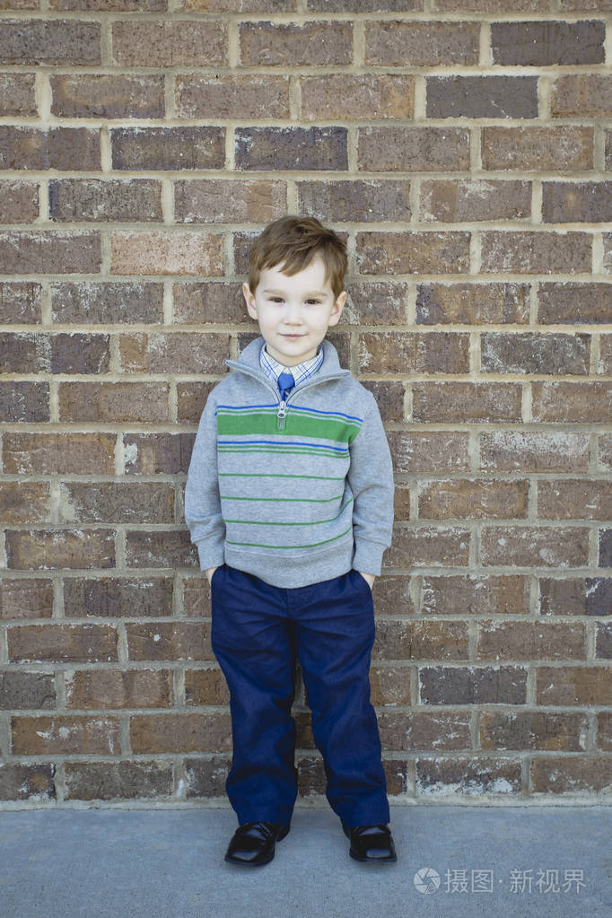 微笑的可爱男孩站起来一堵砖墙