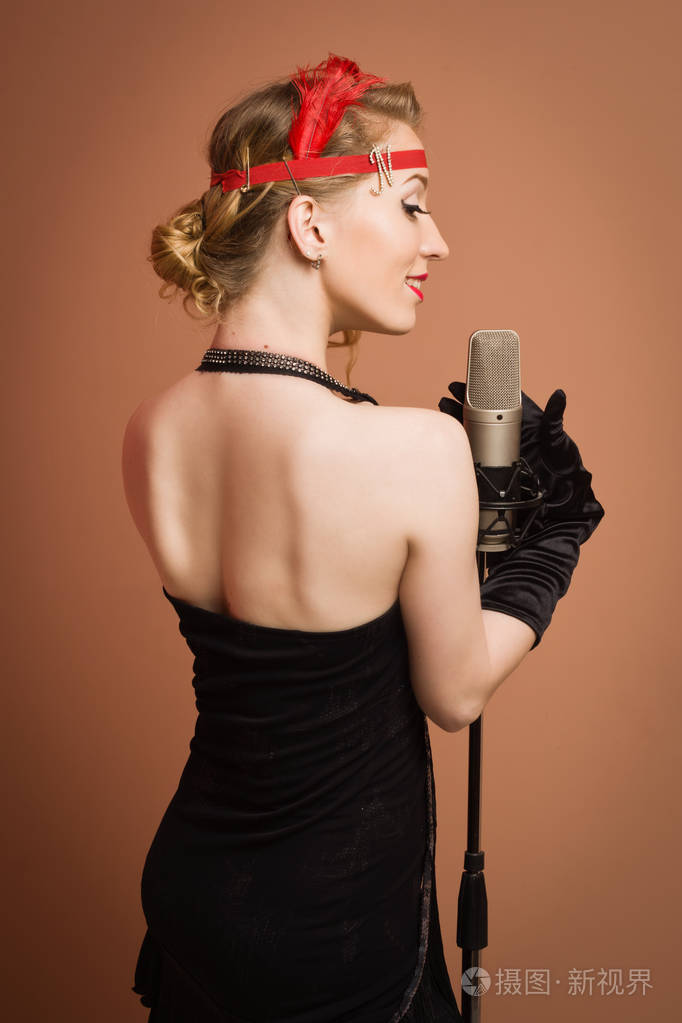 漂亮女演员在黑色复古礼服唱歌与麦克风