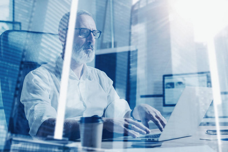 忙着雇主概念的成人胡子商人戴着经典的眼镜和手提电脑在现代接工作室