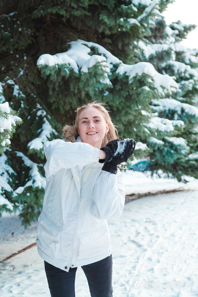 女人与长长的金发,穿着白色夹克玩雪的背景下白雪覆盖的树木和高高兴