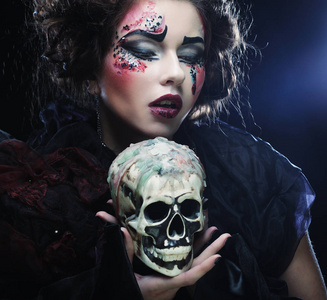 年轻漂亮的女巫,抱着一个骷髅头照片