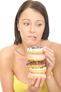 迷人的自然年轻女人拿着一堆冰镇甜甜圈，脸上表情内疚