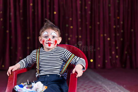 穿着小丑化妆的男孩坐在舞台上的椅子上